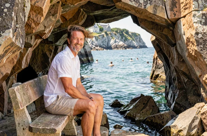 Homme détendu dans une crique bretonne abritée profitant de la fraîcheur littorale pendant un épisode de chaleur, mer bleue et rochers de granit autour de lui
