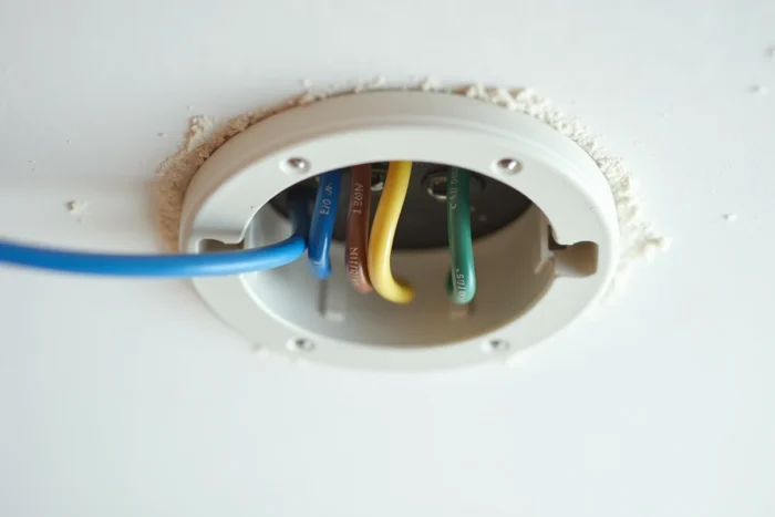 Gros plan sur les trois fils électriques bleu, marron et vert-jaune connectés aux bornes d'un domino de plafond lors de l'installation d'un luminaire